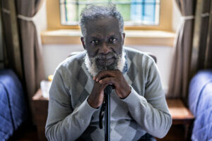 A man who is one of many people with Alzheimer’s stares straight ahead as he leans on a cane.