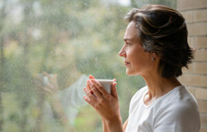 A caregiver sips tea as she looks out the window after experiencing caregiver isolation.