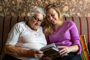 An older woman looks through a photo album with her caregiver to improve memory.