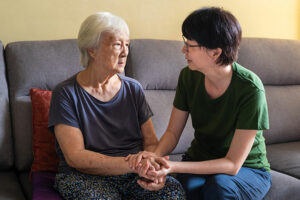 I woman who wonders, “Could Alzheimer’s disease be an autoimmune condition?” holds the hands of her older mother and looks at her with a concerned expression.