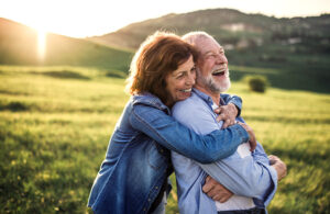 A woman who understands the benefits of hugs for seniors hugs her elderly father as they enjoy the great outdoors together.