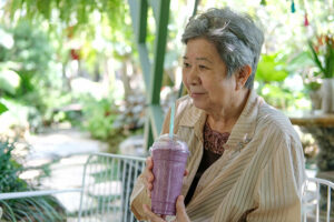 An older woman sits outside enjoying a smoothie, one of many effective dysphagia tips to help with using beverage thickeners.