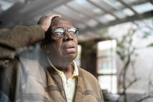 An older man experiencing restlessness in dementia holds his head and gazes out the window.