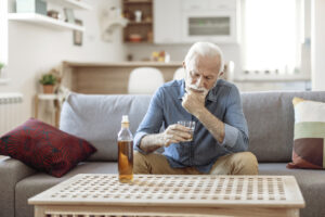 An older man showing signs of substance misuse in older adults holds a glass of whiskey.