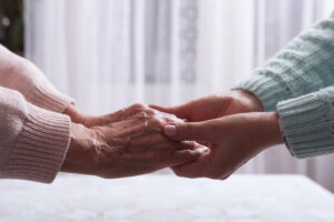 A younger woman holds the hands of her older mother to show how she is supporting mental health in aging parents.