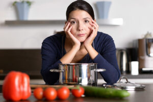 A woman who is feeling bored as a caregiver leans on her hands before preparing a meal.