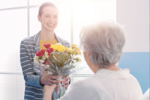 An older woman who required a temporary assisted living stay receives a visit and flowers from her daughter.