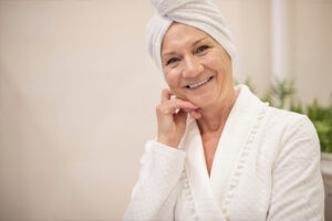 A woman wearing a robe and head towel smiles as she considers whether daily bathing for seniors is best.