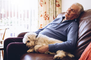 A man experiencing chronic fatigue in older adults naps on the couch with his dog by his side.