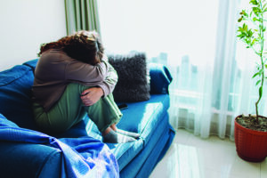 A woman struggling with caregiver PTSD sits on the sofa with her face covered.