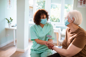 masked caregiver providing in-home recovery care for senior client
